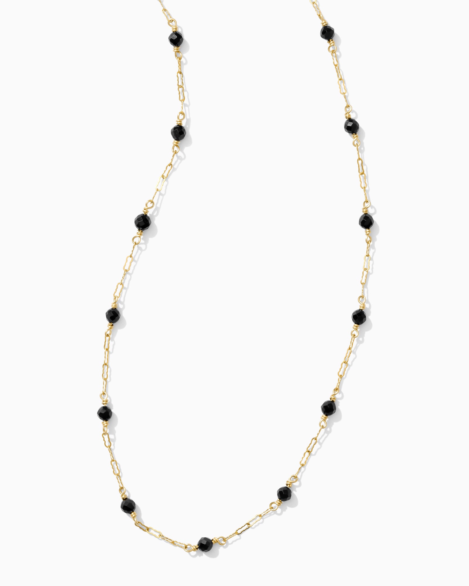 Necklace with black beads on a gold chain against a white background.
