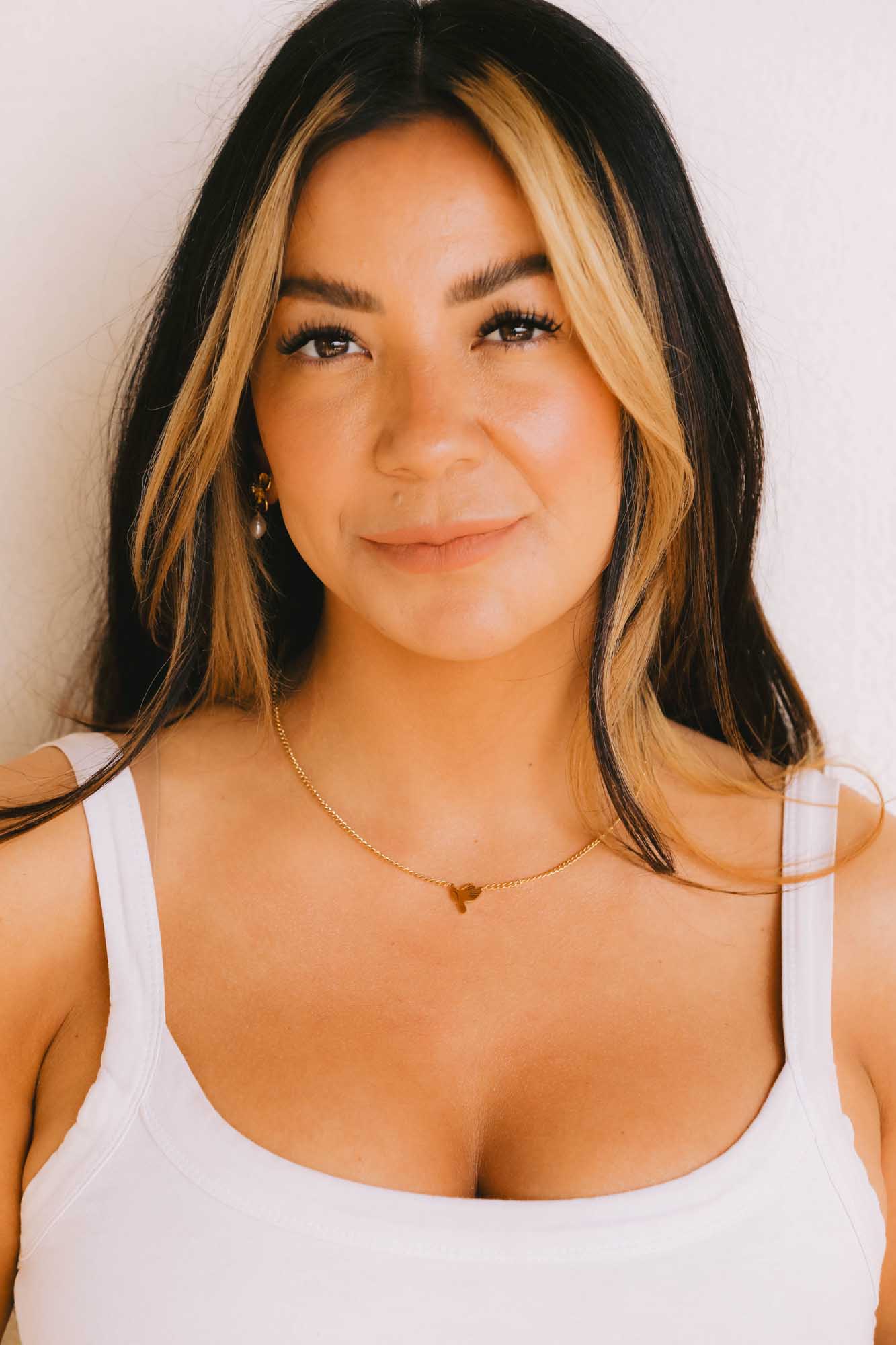 Woman wearing a white tank top and a gold necklace on a white background.