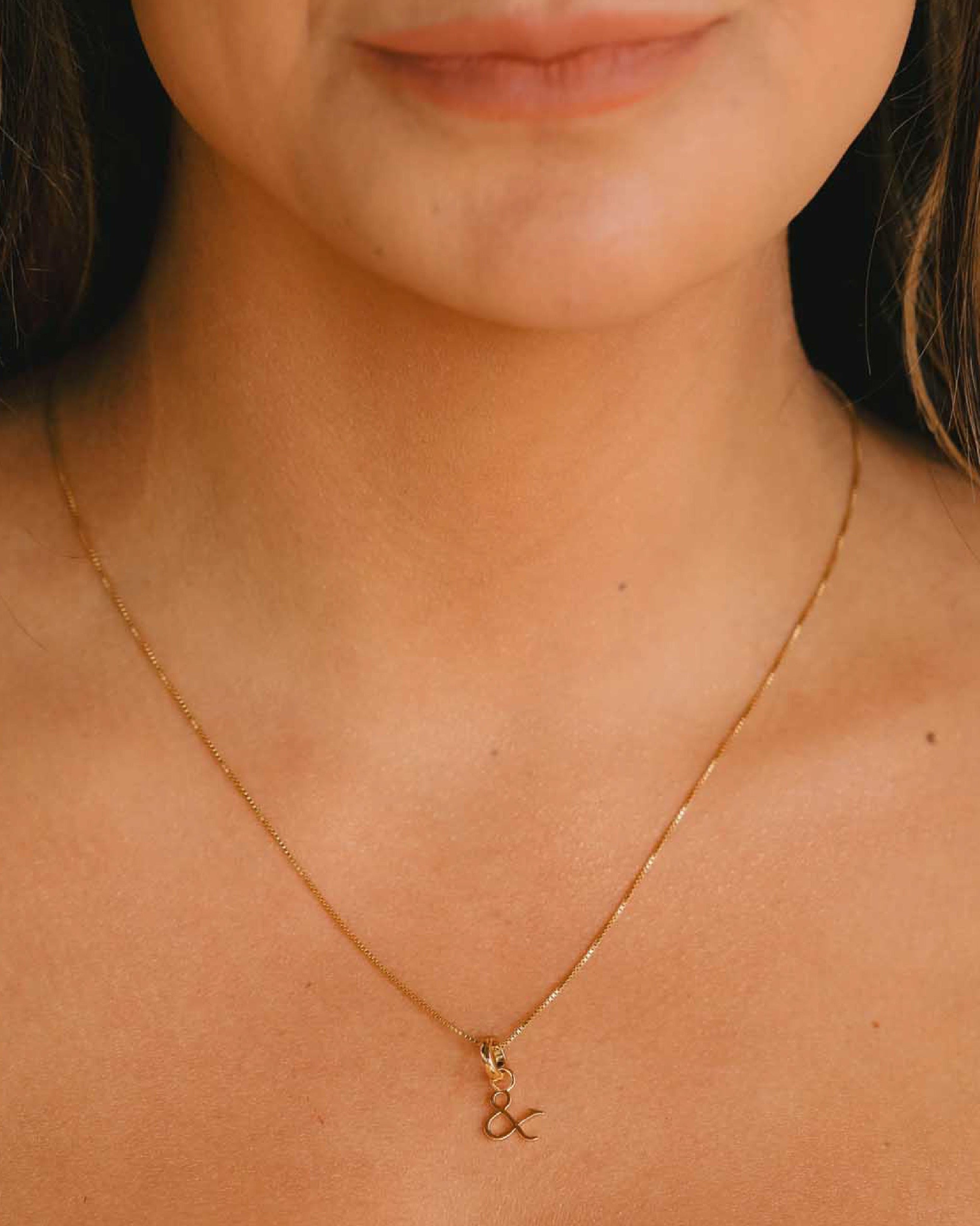 Close-up of a person wearing a gold necklace with a small gold pendant hanging on a neck of a woman.