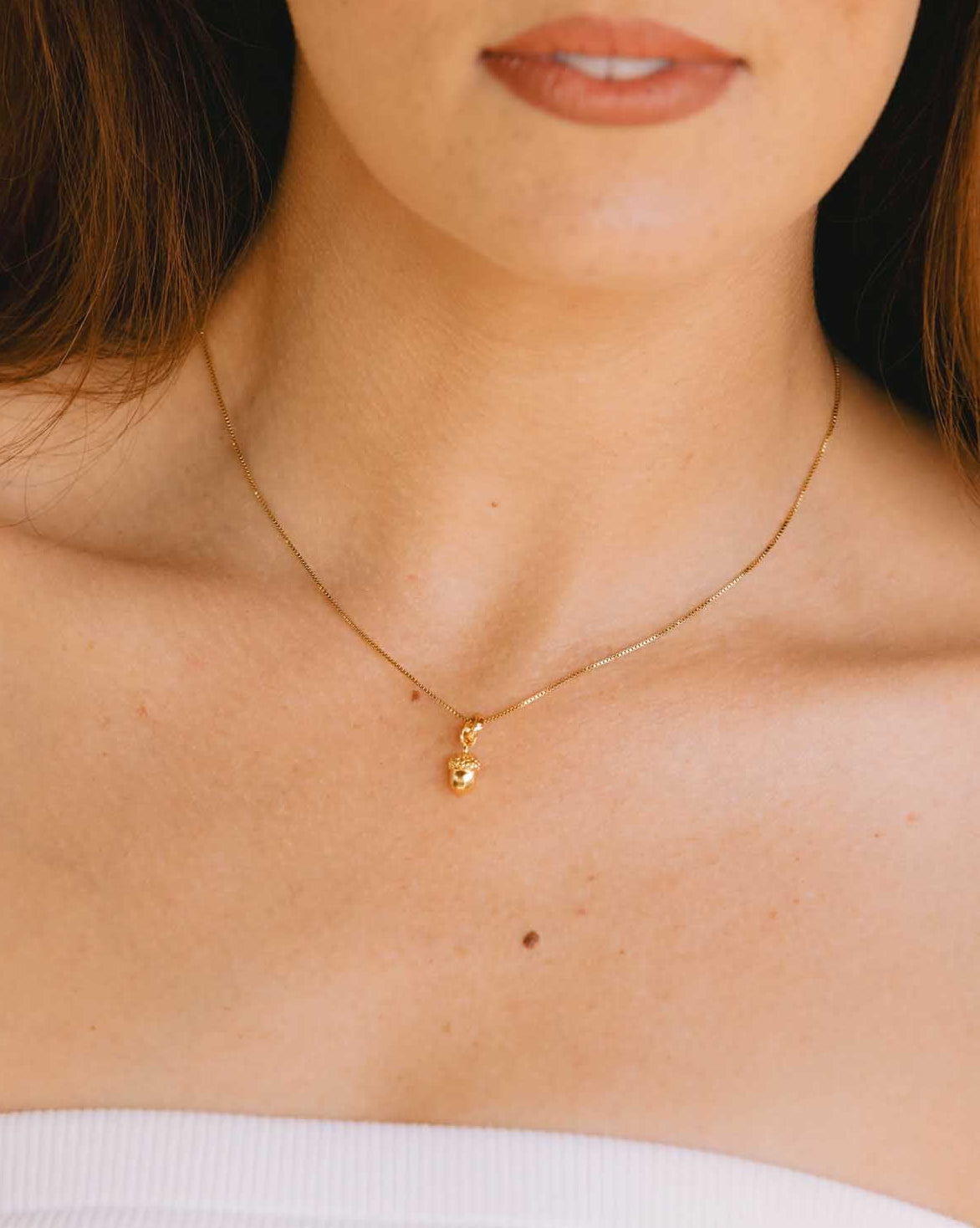 Close-up of a person wearing a gold necklace with a small gold pendant.