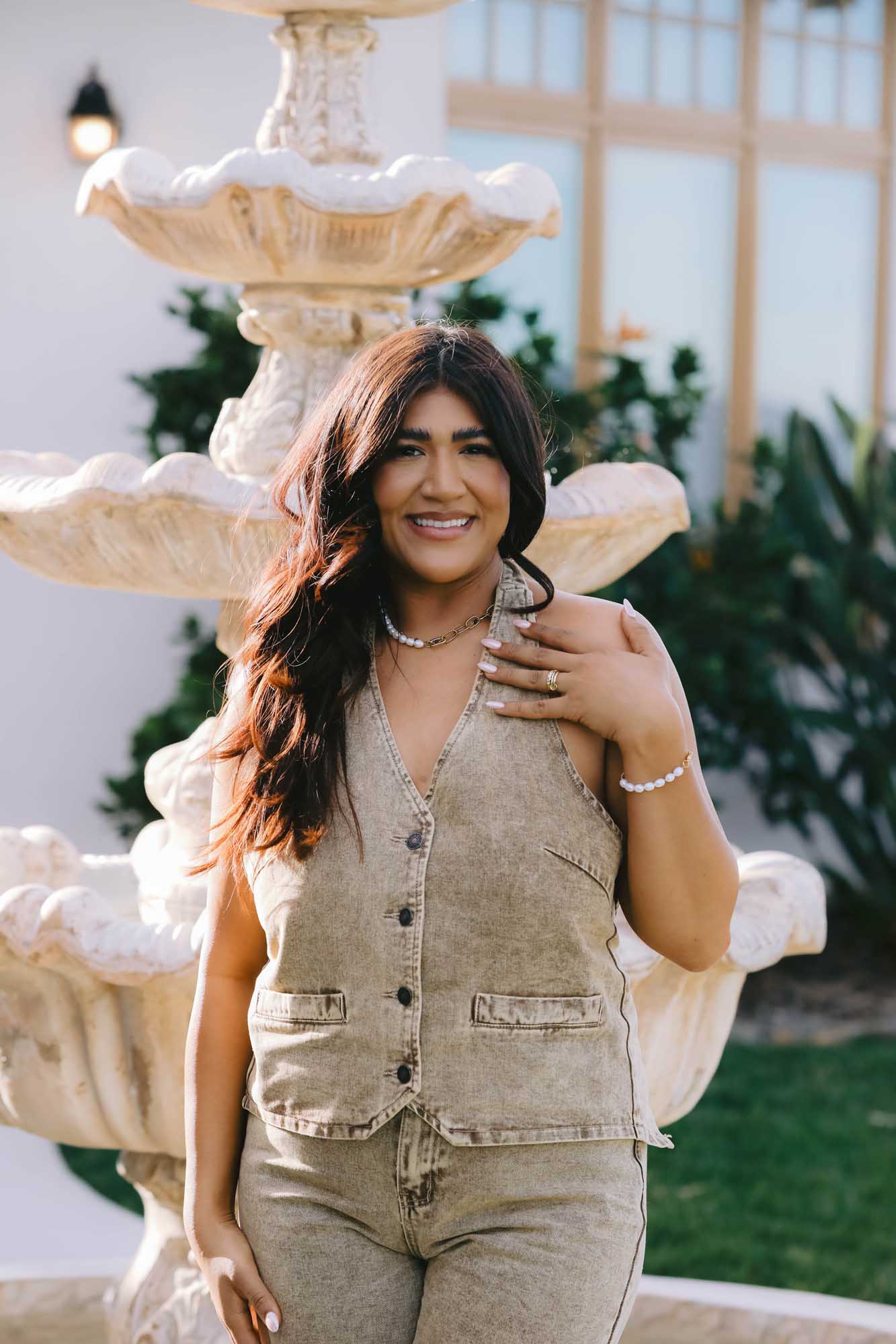 Woman posing in front of a fountain wearing a gold and pearl necklace, gold and pearl bracelet, and gold ring.