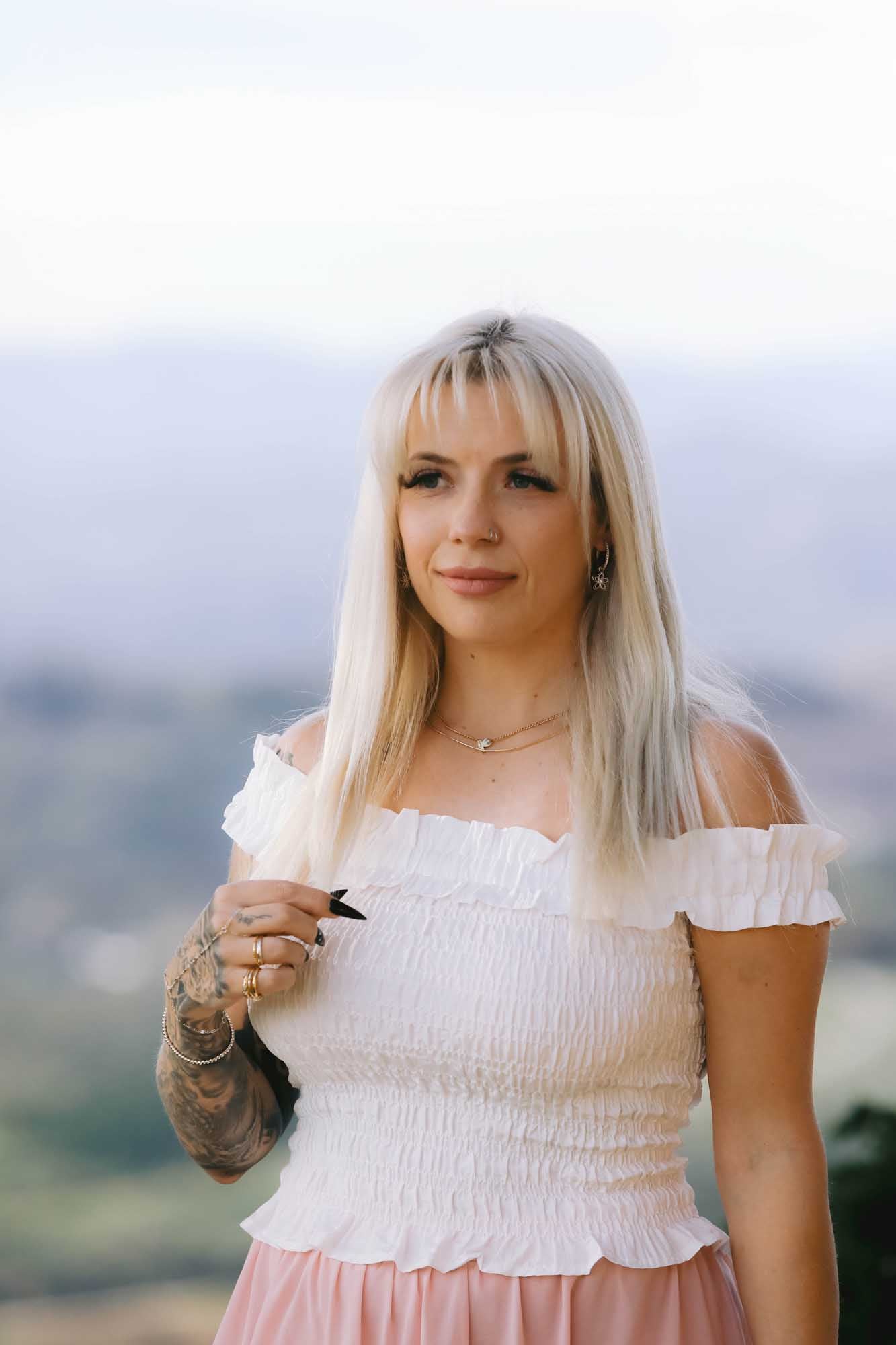 Woman wearing multiple necklace, multiple bracelets, and multiple rings on a blurred white background.