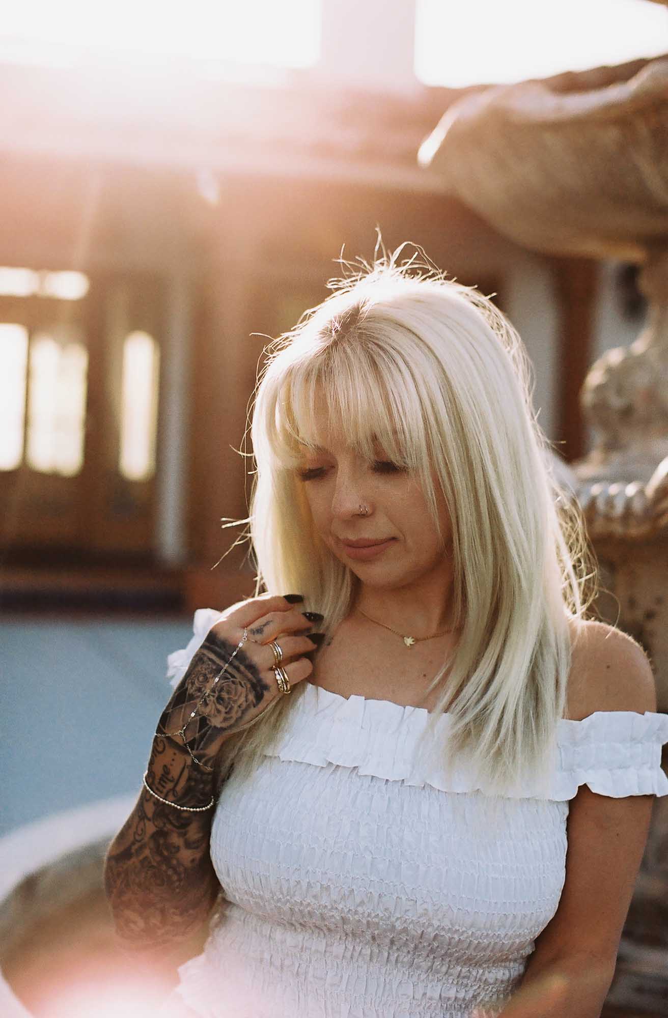 Woman thinking while wearing a gold necklace, silver bracelet, and mixed gold and silver rings while sunlight shines