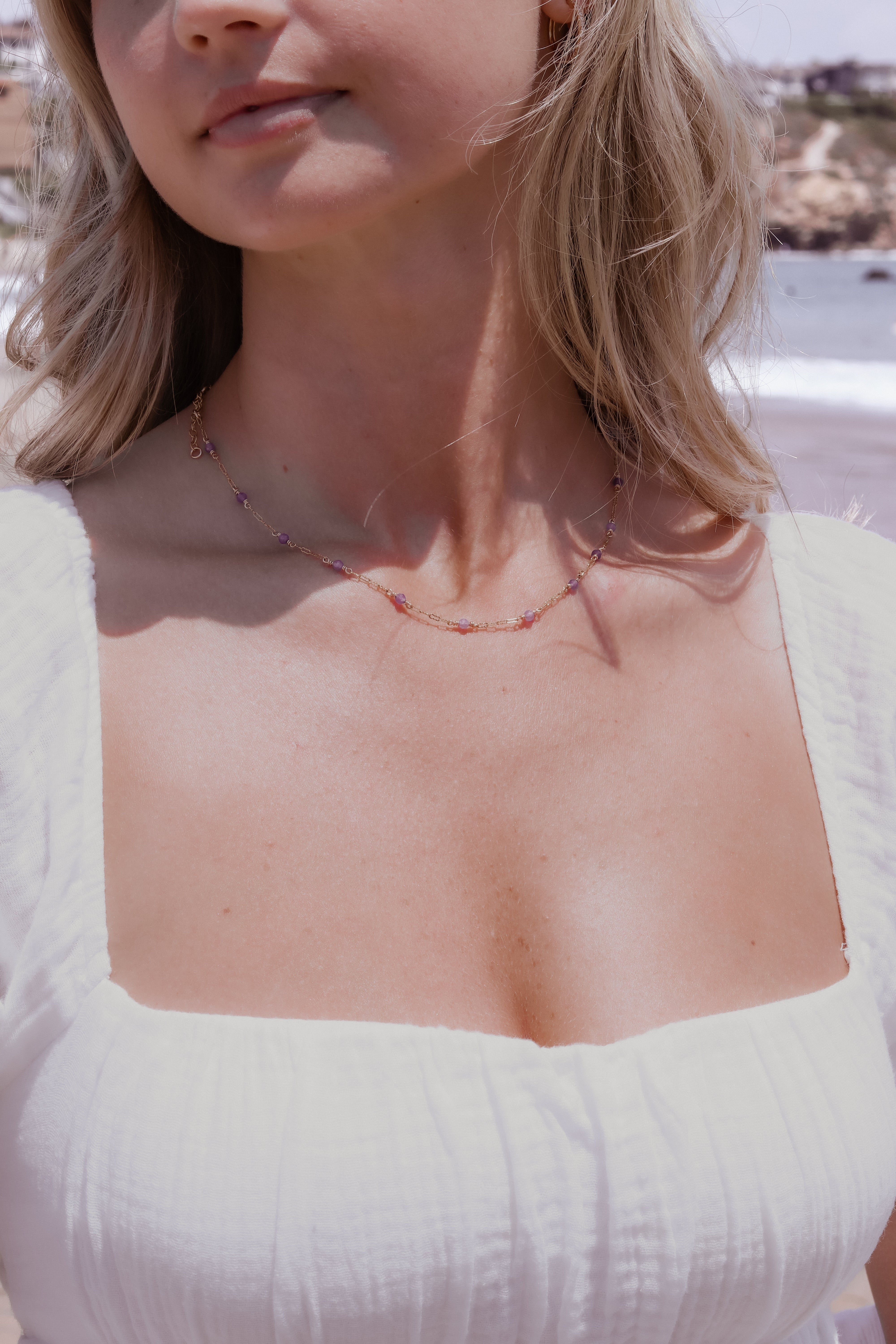 Woman wearing a white top with a clear design and a gold beaded necklace standing outdoors.