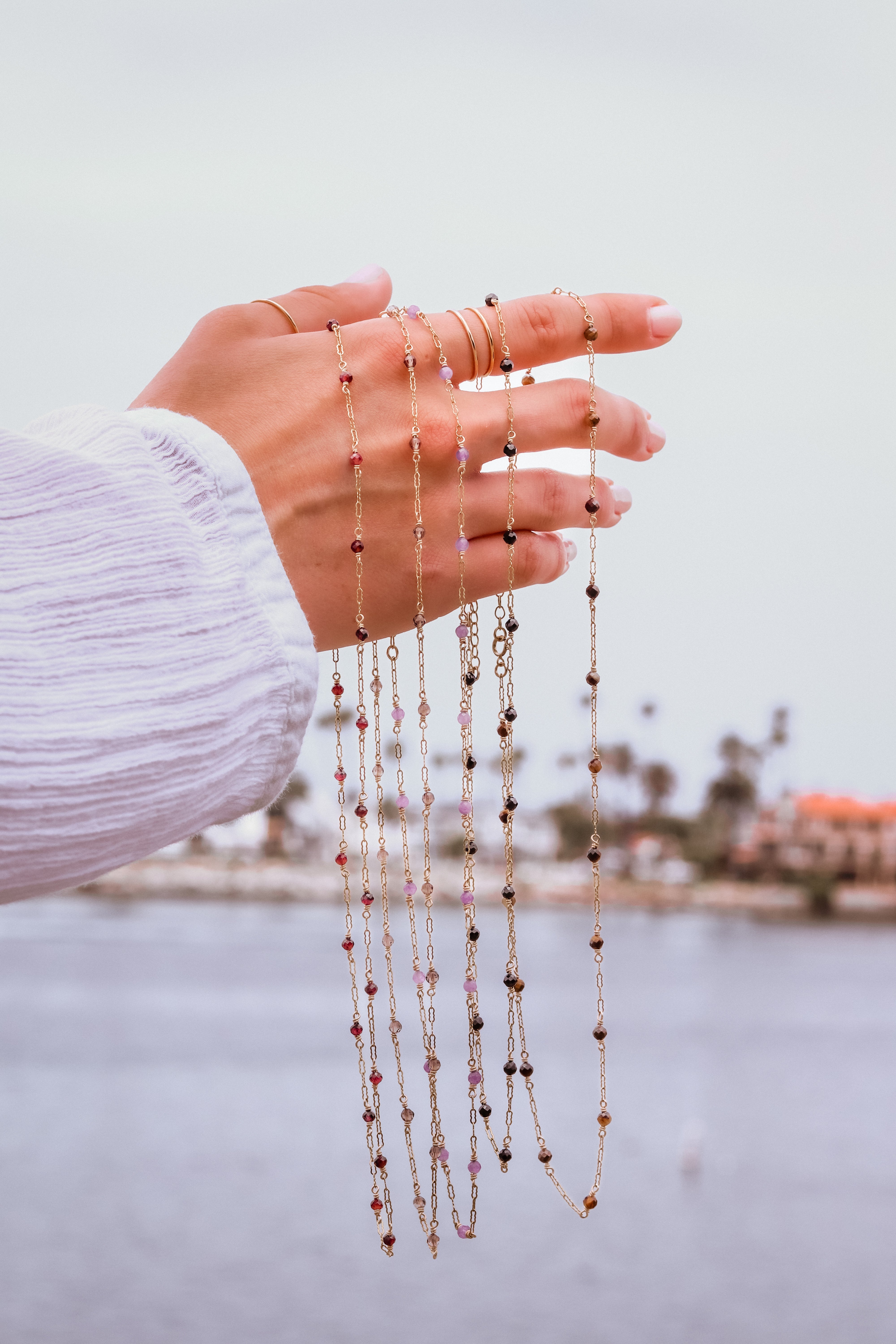 Hand holding multiple gold beaded necklace with a blurred outdoor background.