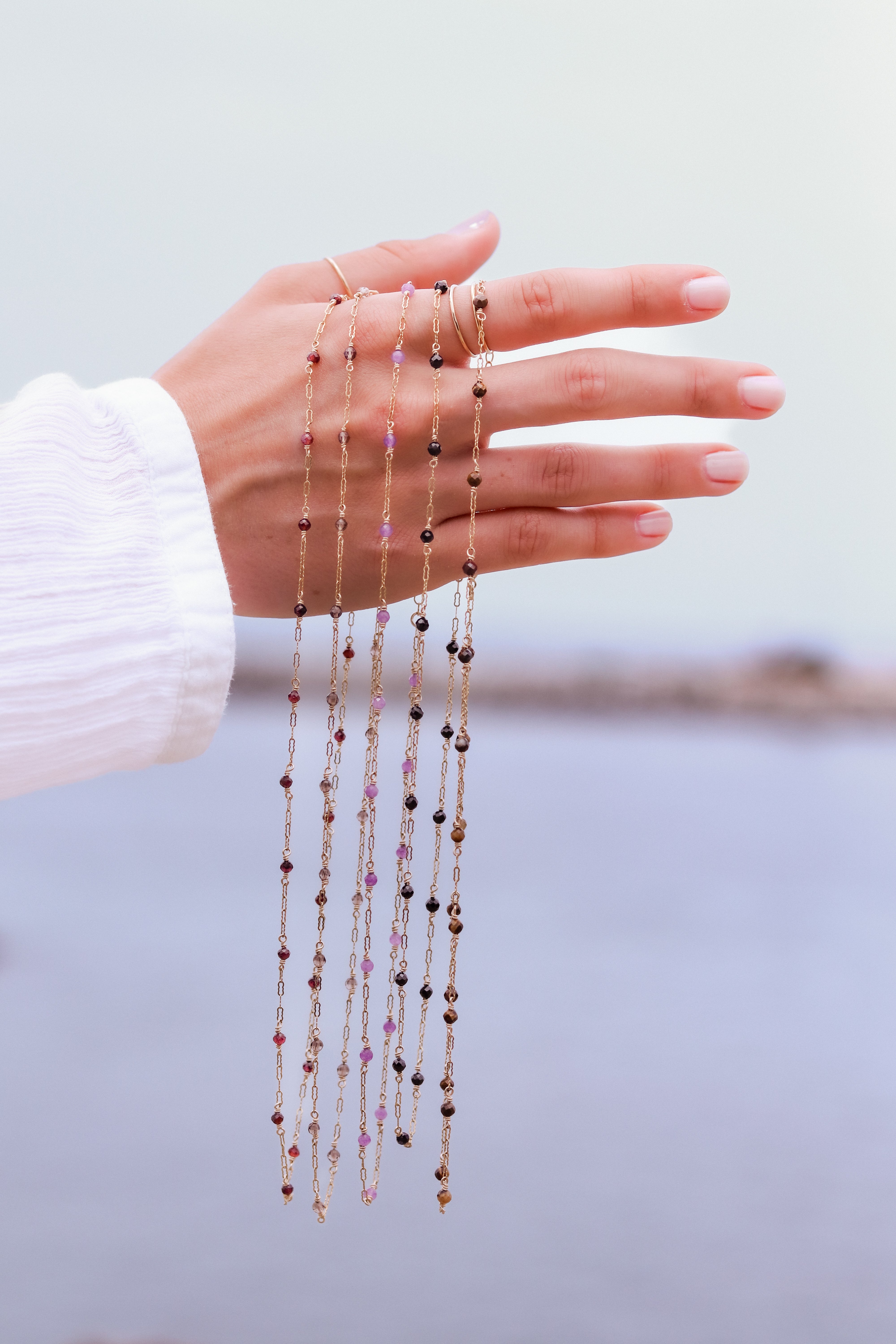Close-up of a hand holding multiple gold beaded necklace against a light background.
