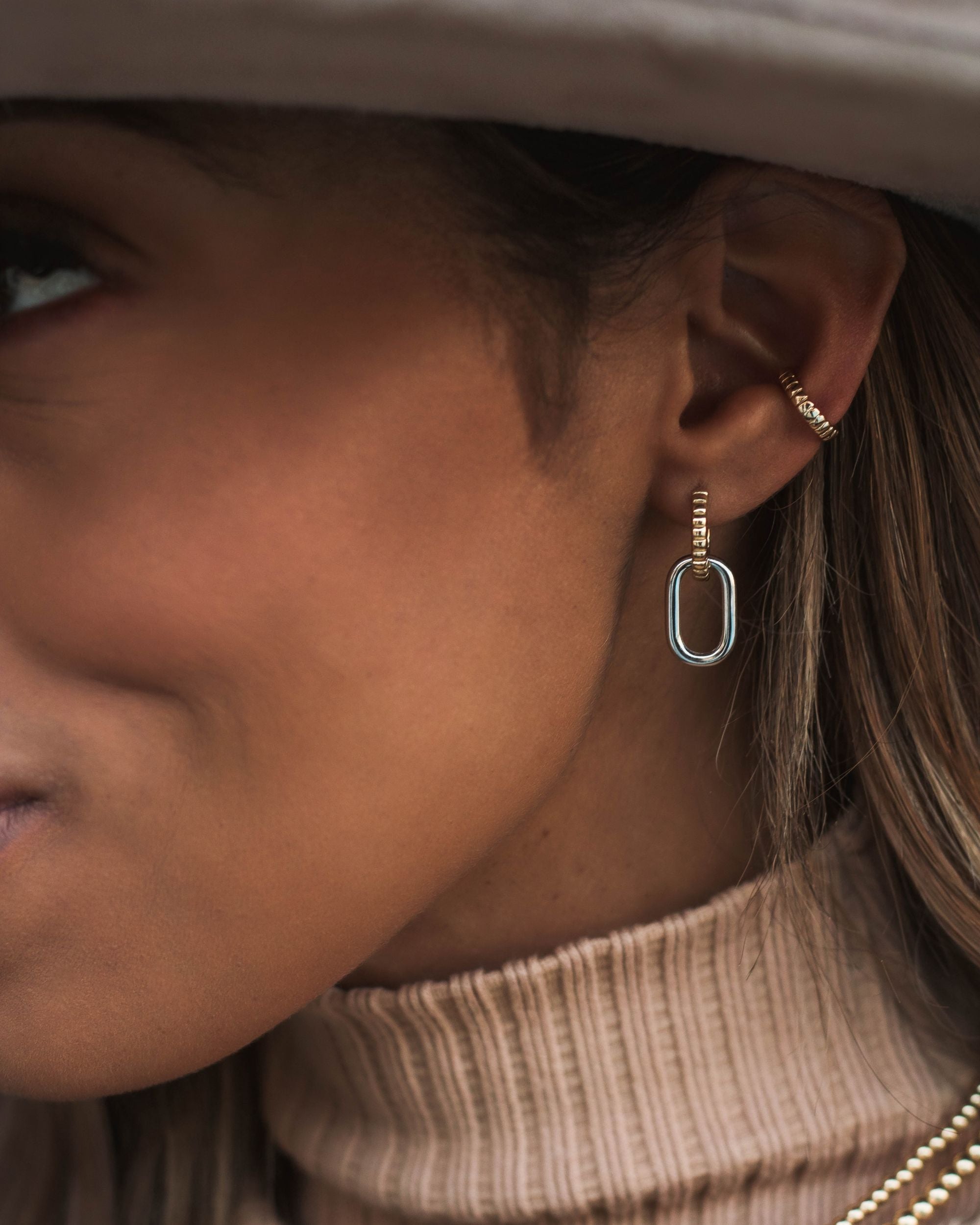 A close-up of an ear wearing one hooped earrings that forms in a 'C' and the other has a silver paperclip type design hanging.