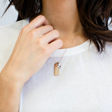 A woman models a gold necklace with personalized bars and a heart with a paw that dangle around her neck.