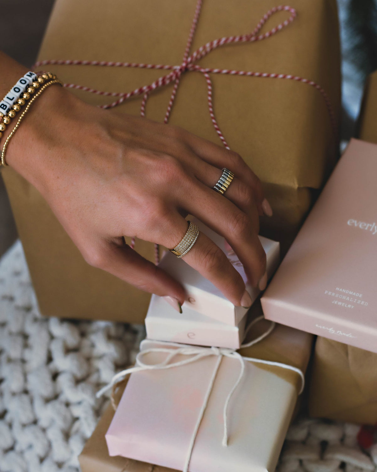 A background of multiple packages of different sizes with a hand over the boxes wearing two gold rings and multiple gold bracelets on the wrist.