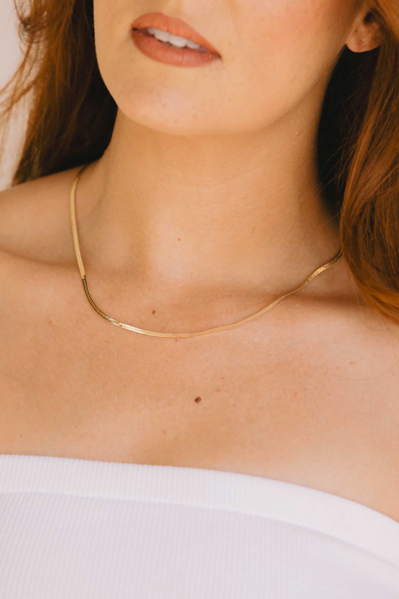 Gold necklace on a person wearing a white strapless top.