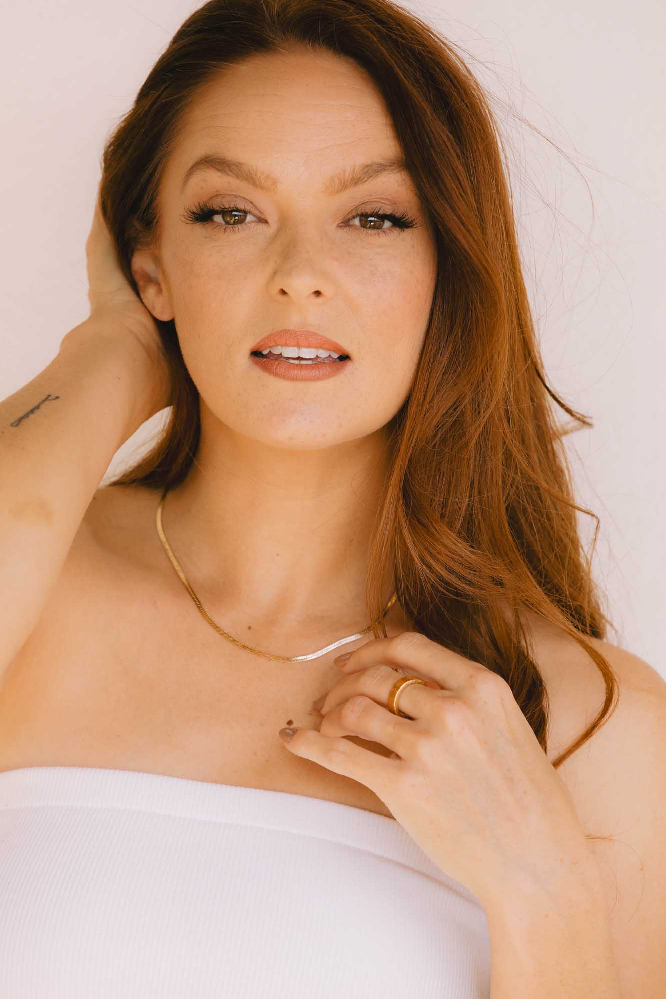 Woman wearing a gold necklace and gold ring against a white background.