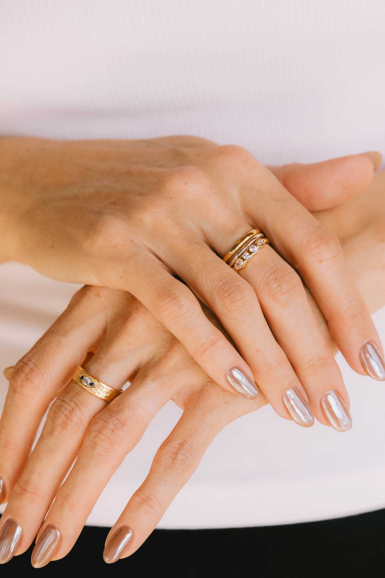Close-up of two manicured hands adorned with gold rings on a white background