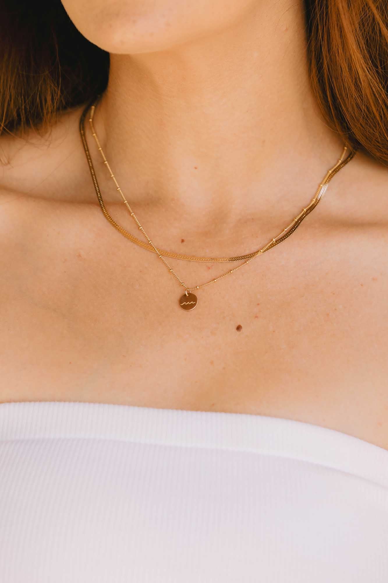 Close-up of a person wearing two gold necklaces one with a pendant on a plain background.
