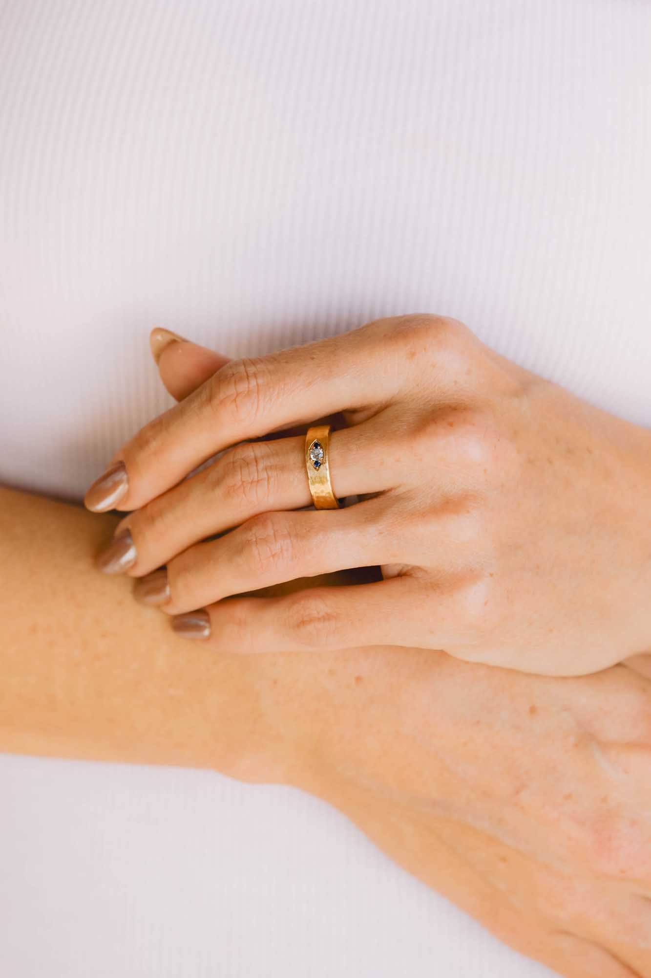 Close-up of a manicured hand wearing a gold ring on a white background