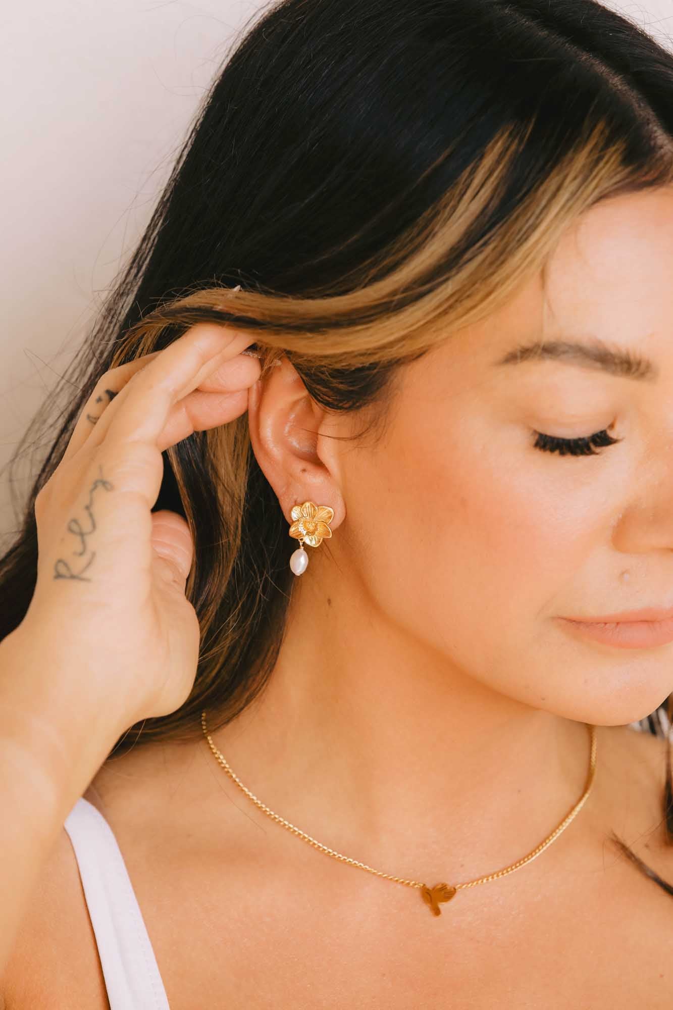 Woman wearing gold earrings and a gold necklace, adjusting her hair to show her earrings