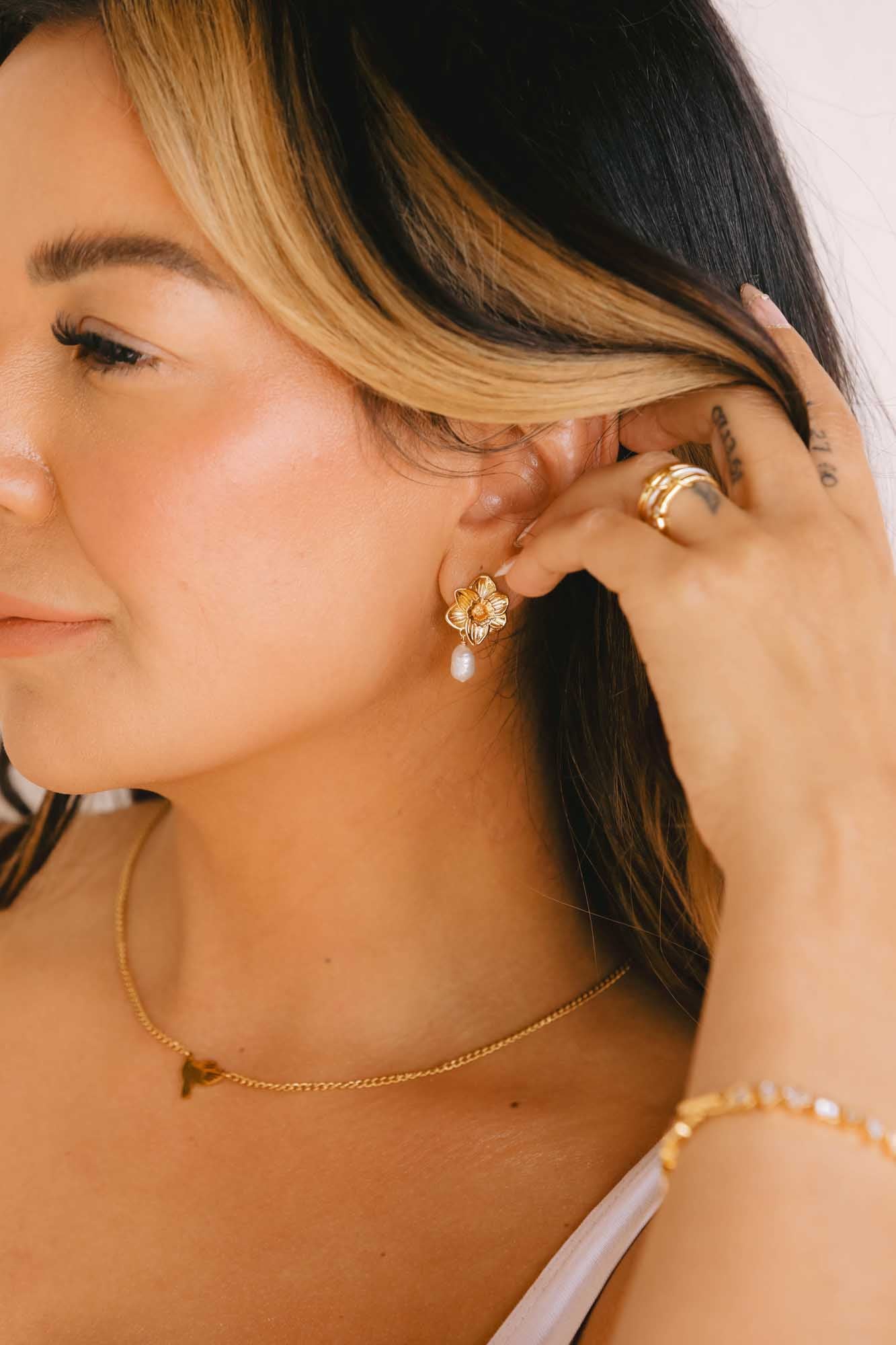 Woman wearing gold earrings, gold ring, gold necklace, and a blurred gold bracelet holding her hair