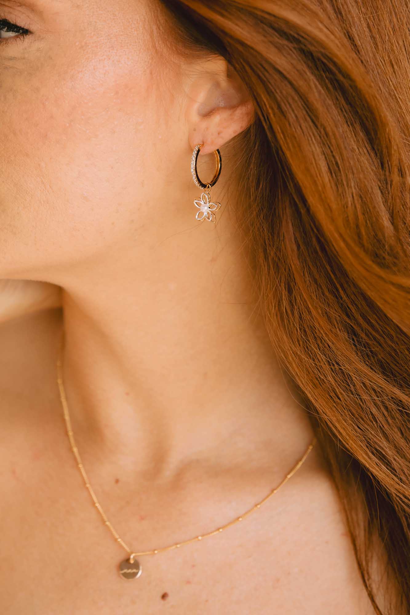 Close-up of a woman wearing gold hoop earrings with a star and a gold necklace with a heart pendant.