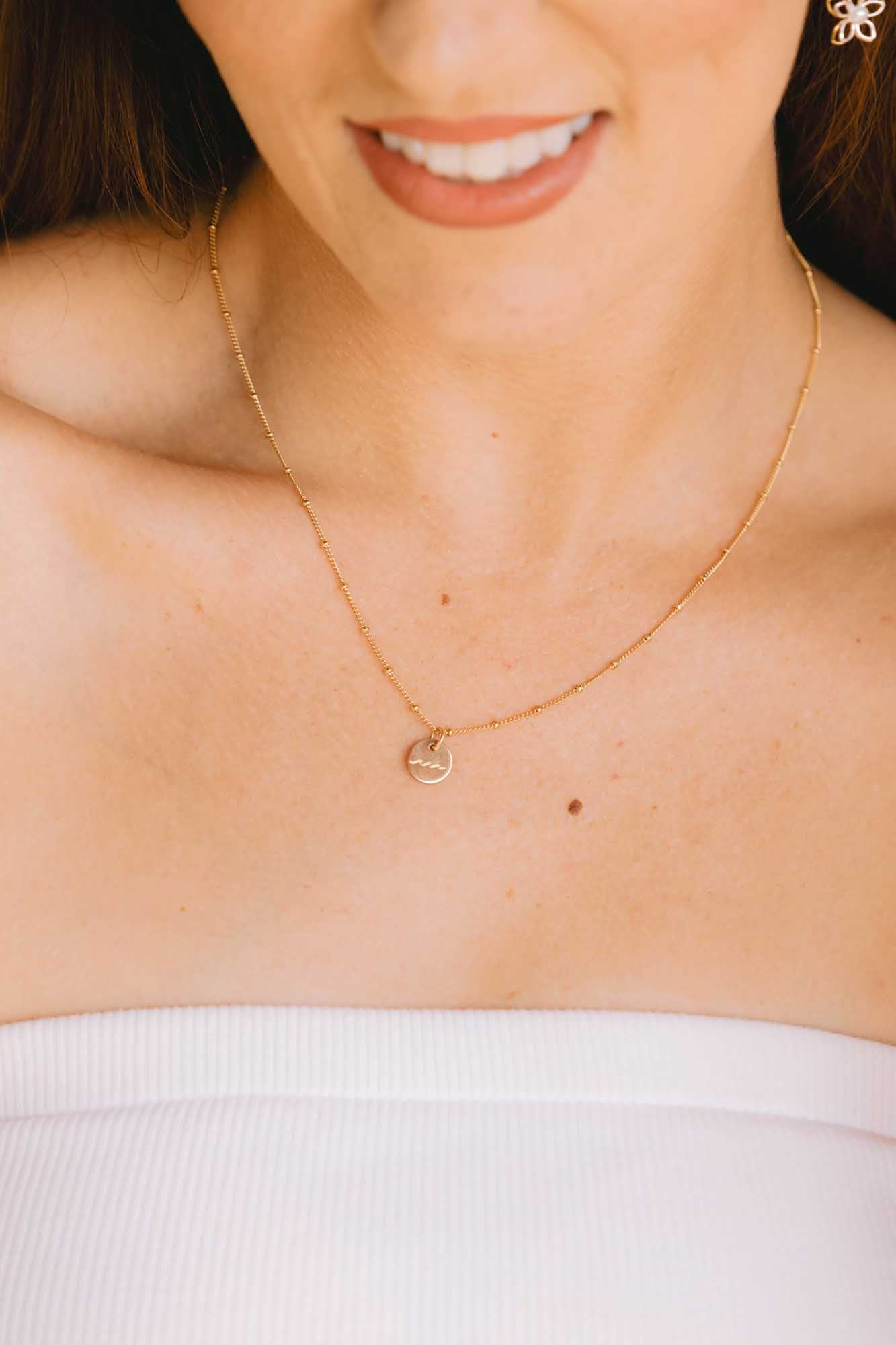 Close-up of a person wearing a gold necklace with a heart-shaped pendant.