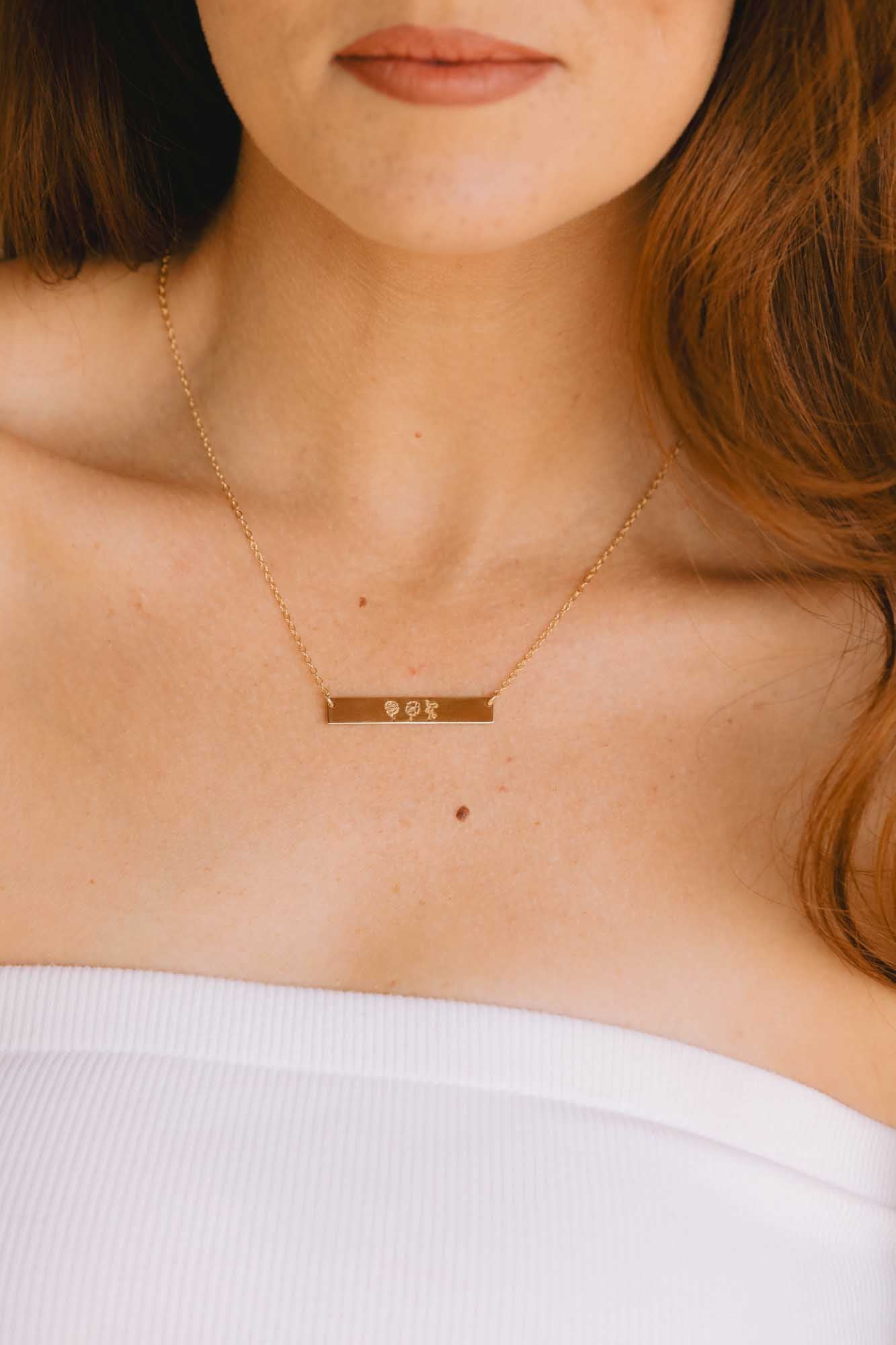 Close-up of a person wearing a gold necklace with a bar pendant.