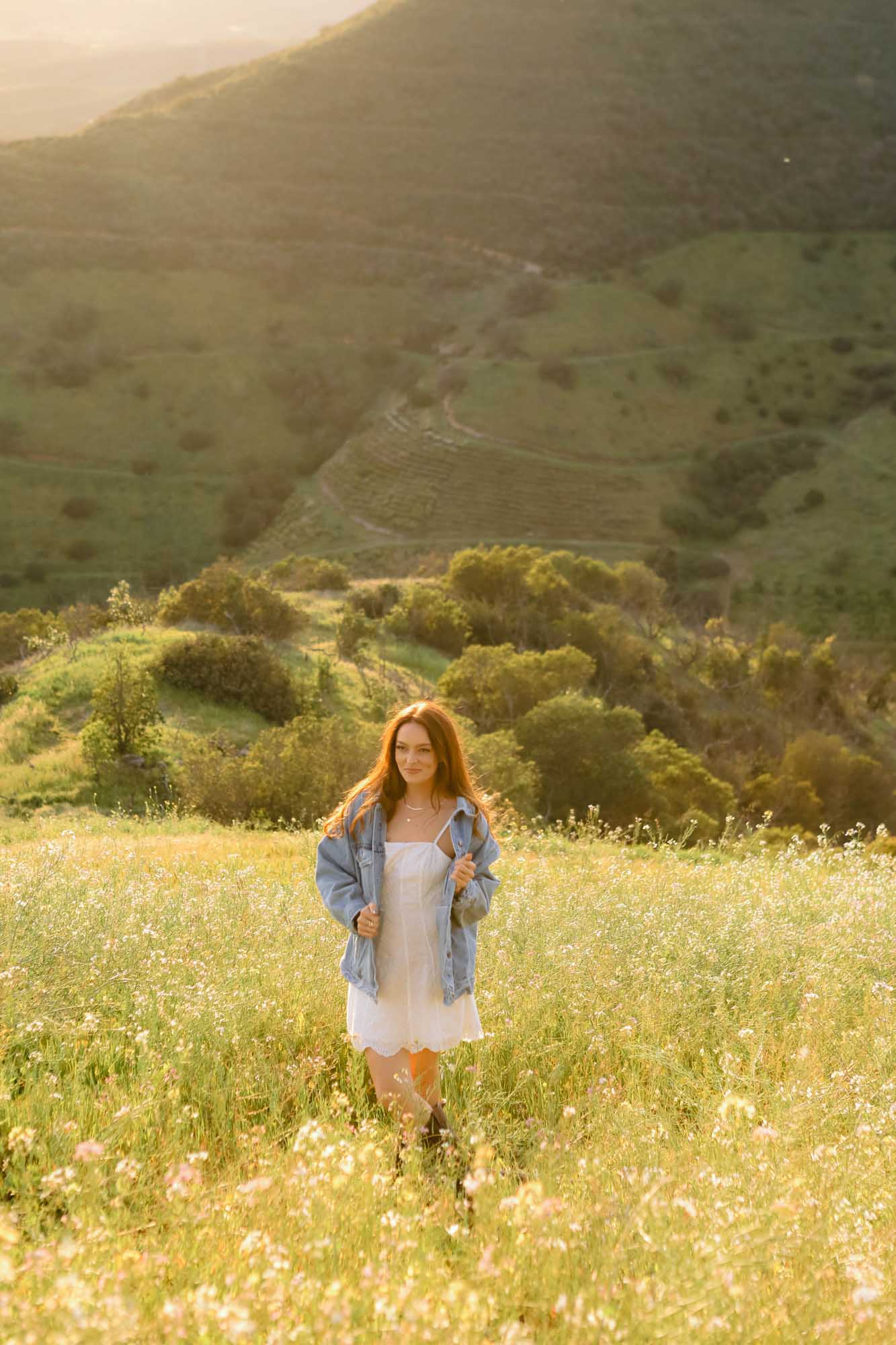 Woman standing in a field with mountains in the background wearing  a gold necklace.