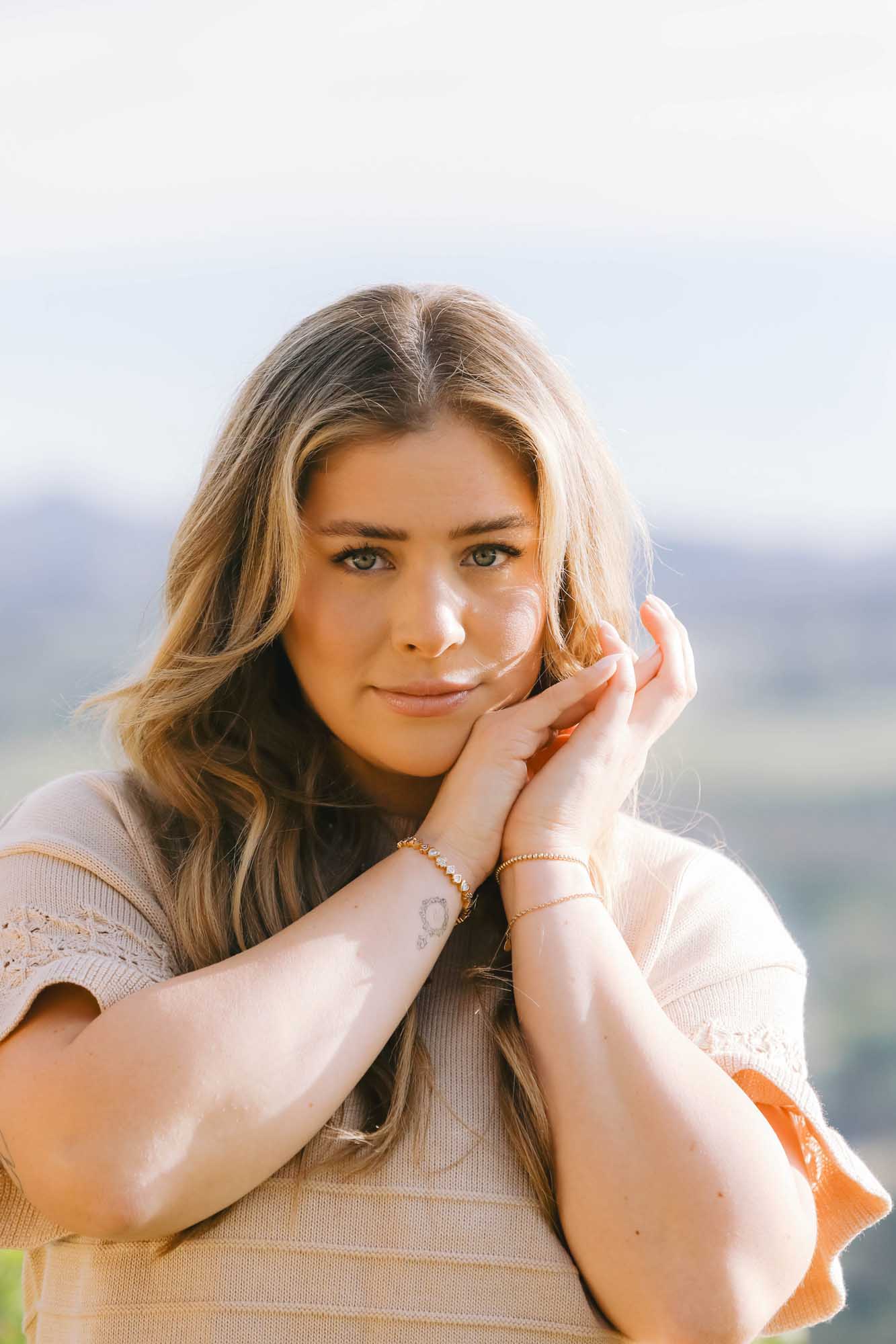 Woman with long blonde hair holding her hands to her face wearing gold bracelets on each wrist