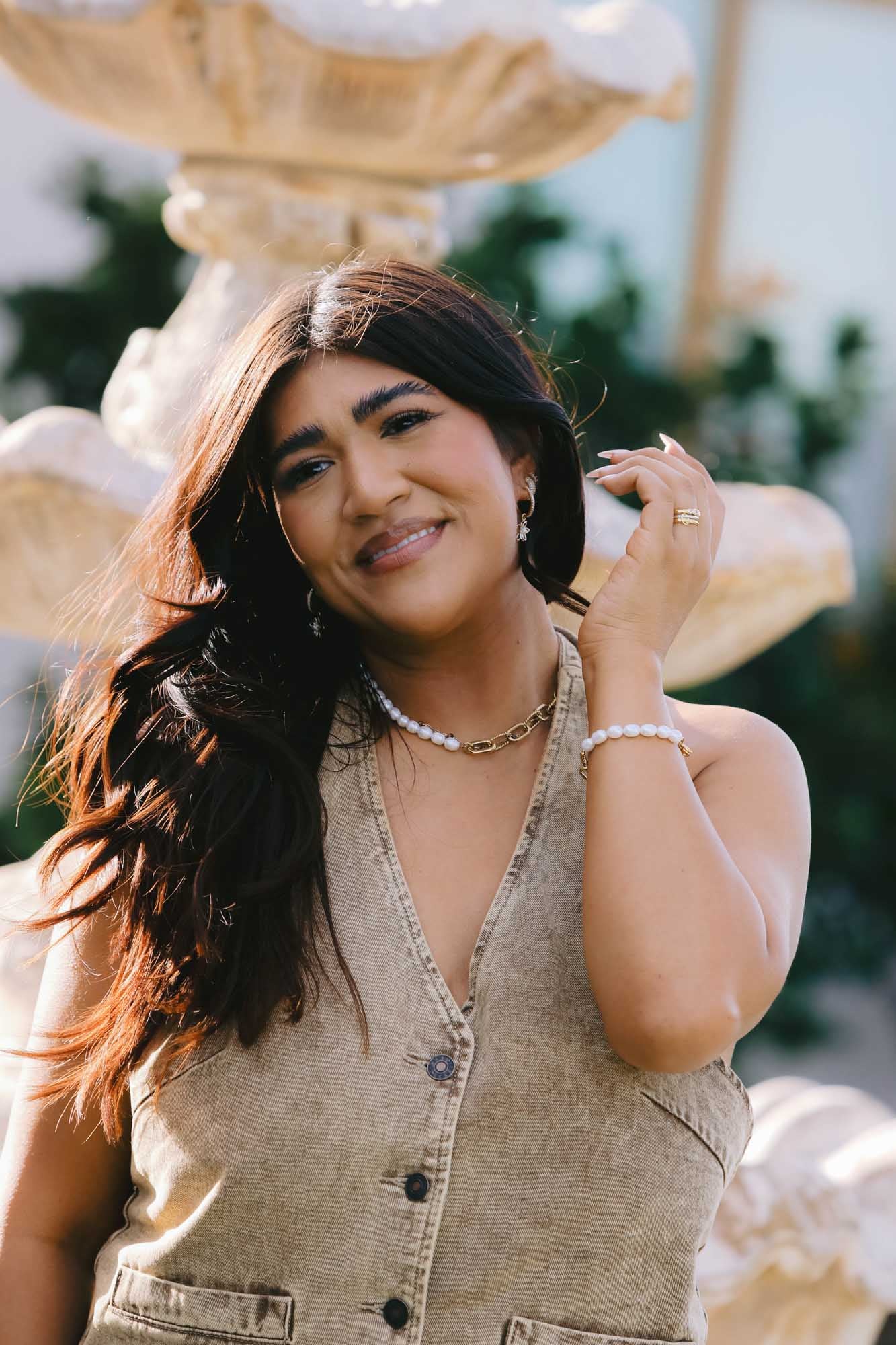 Woman standing in front of a fountain wearing a matching gold and pearl necklace and bracelet.