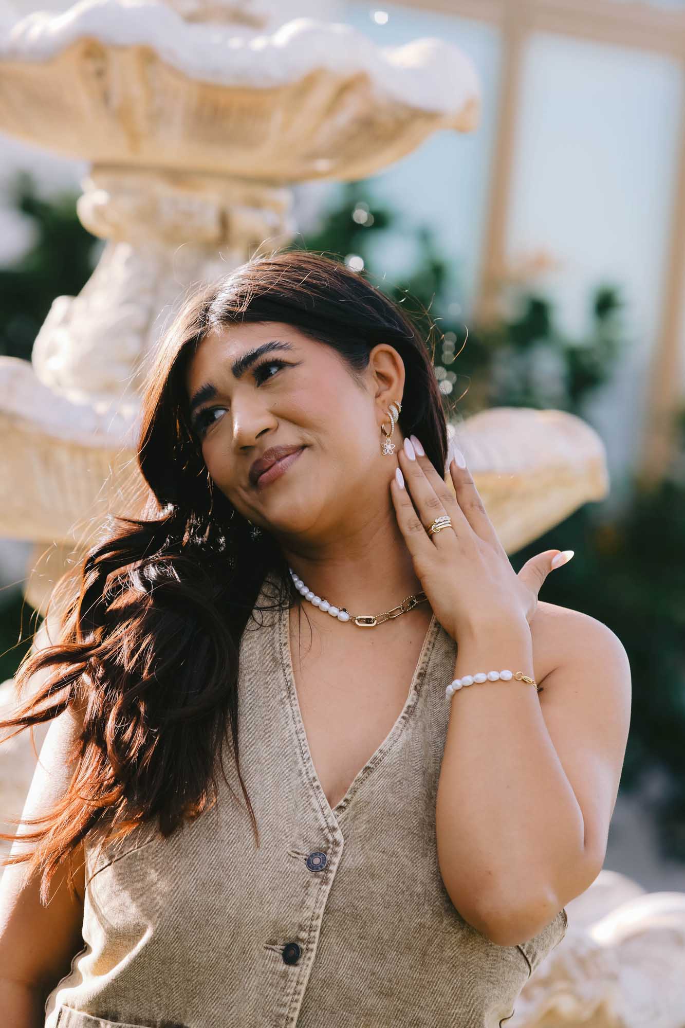 Woman in front of a fountain wearing a matching set of earrings, bracelet, and necklace made of gold and pearls