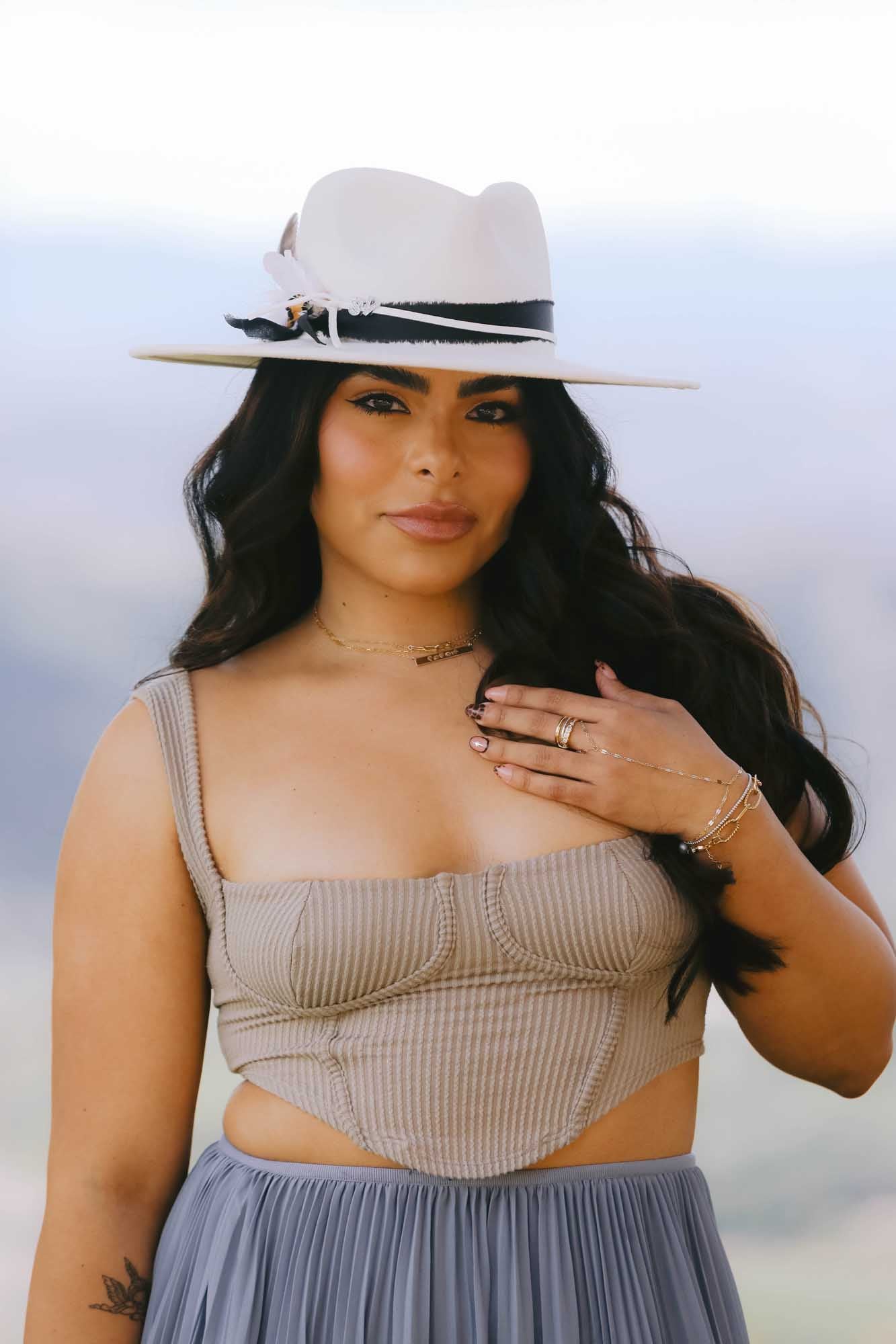Woman with white hat posing with multiple bracelets, rings, and bracelet on a blurred background