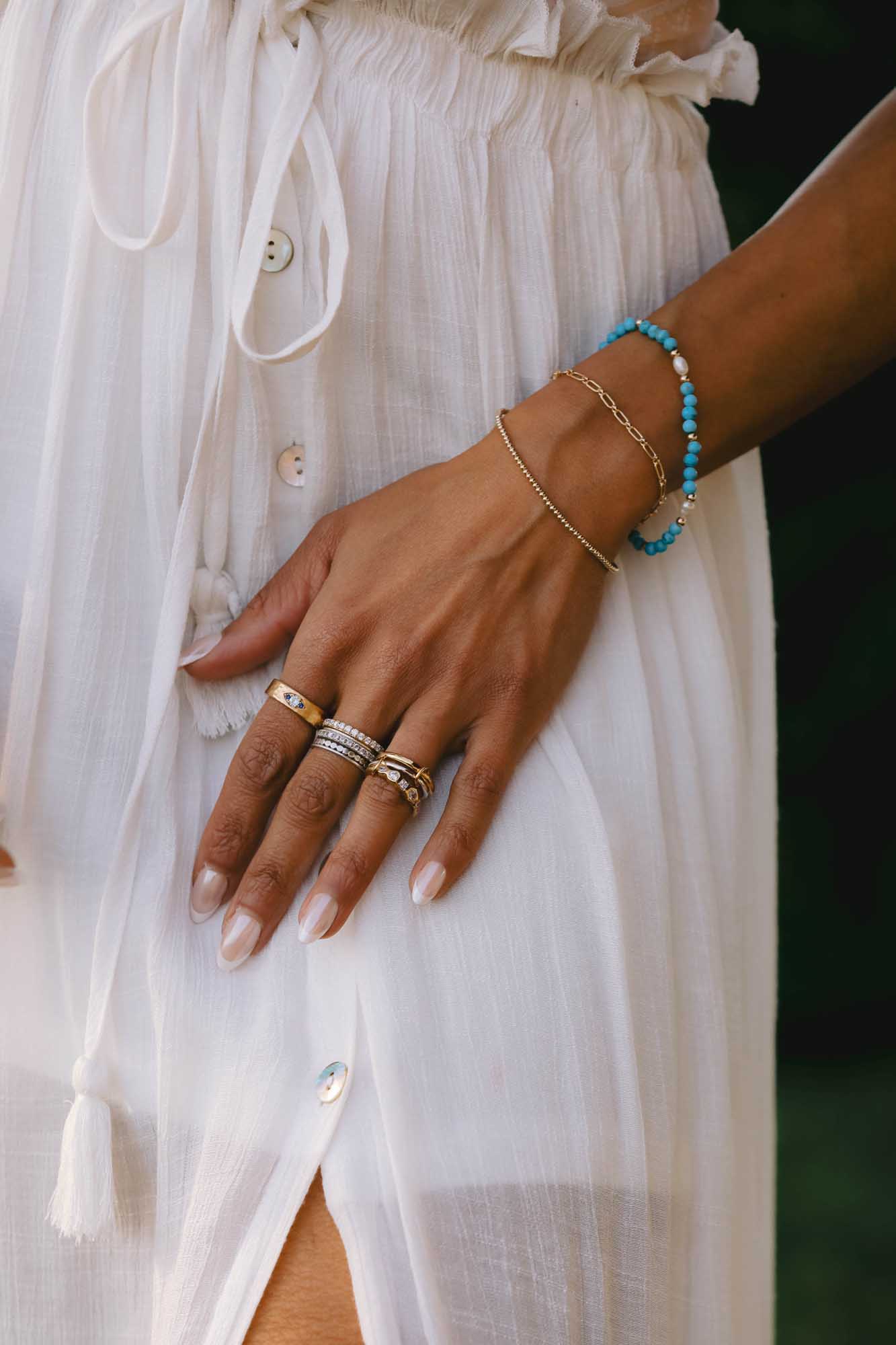 Close-up of a hand wearing multiple rings and bracelets with white dress as background