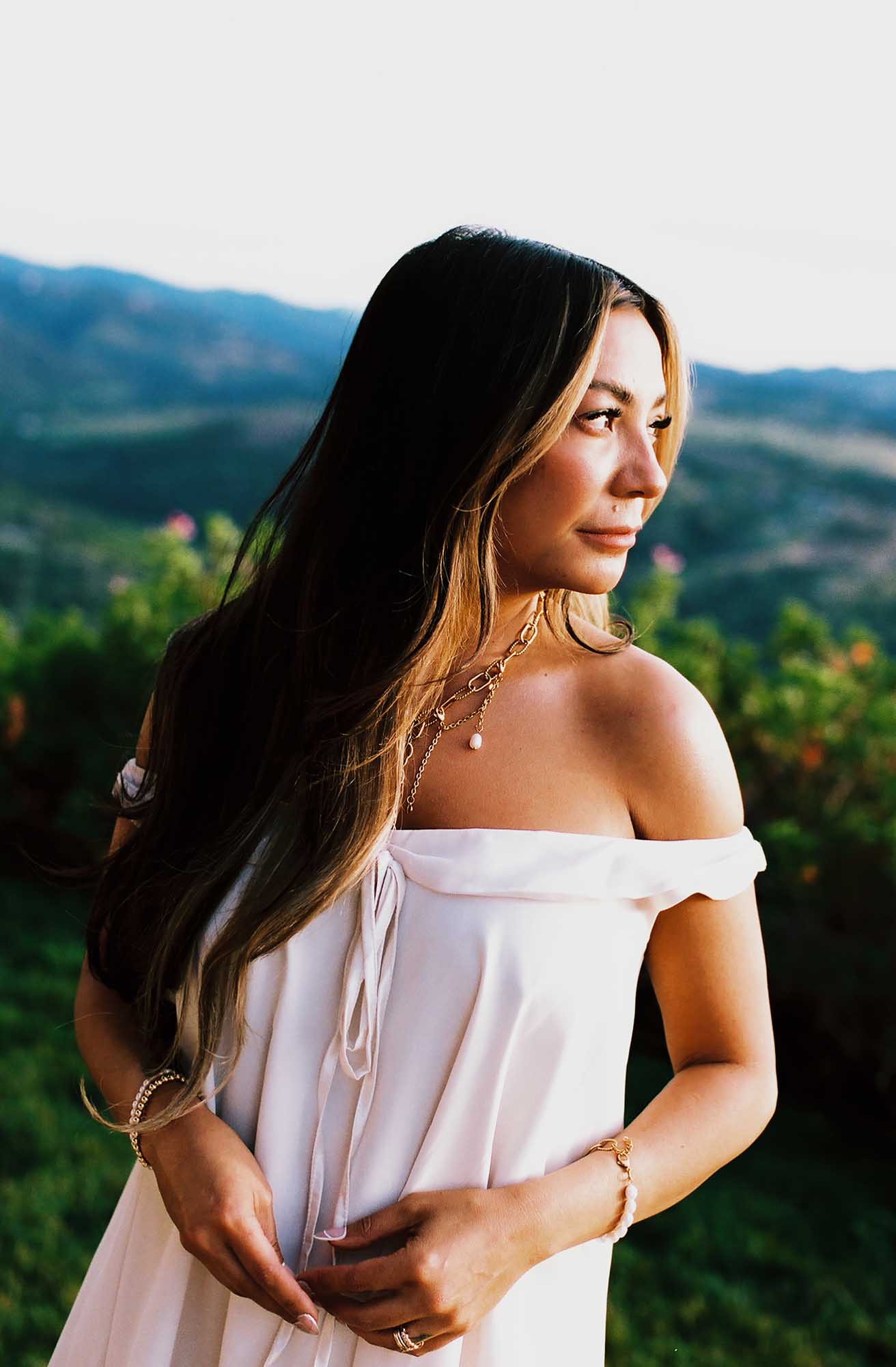 Woman wearing multiple gold and pearl necklace, gold ring, multiple gold and pearl bracelets on each wrist.