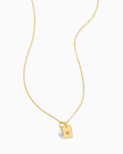 Gold necklace with a pendant featuring a pearl and engraved letter 'R' on a white background.